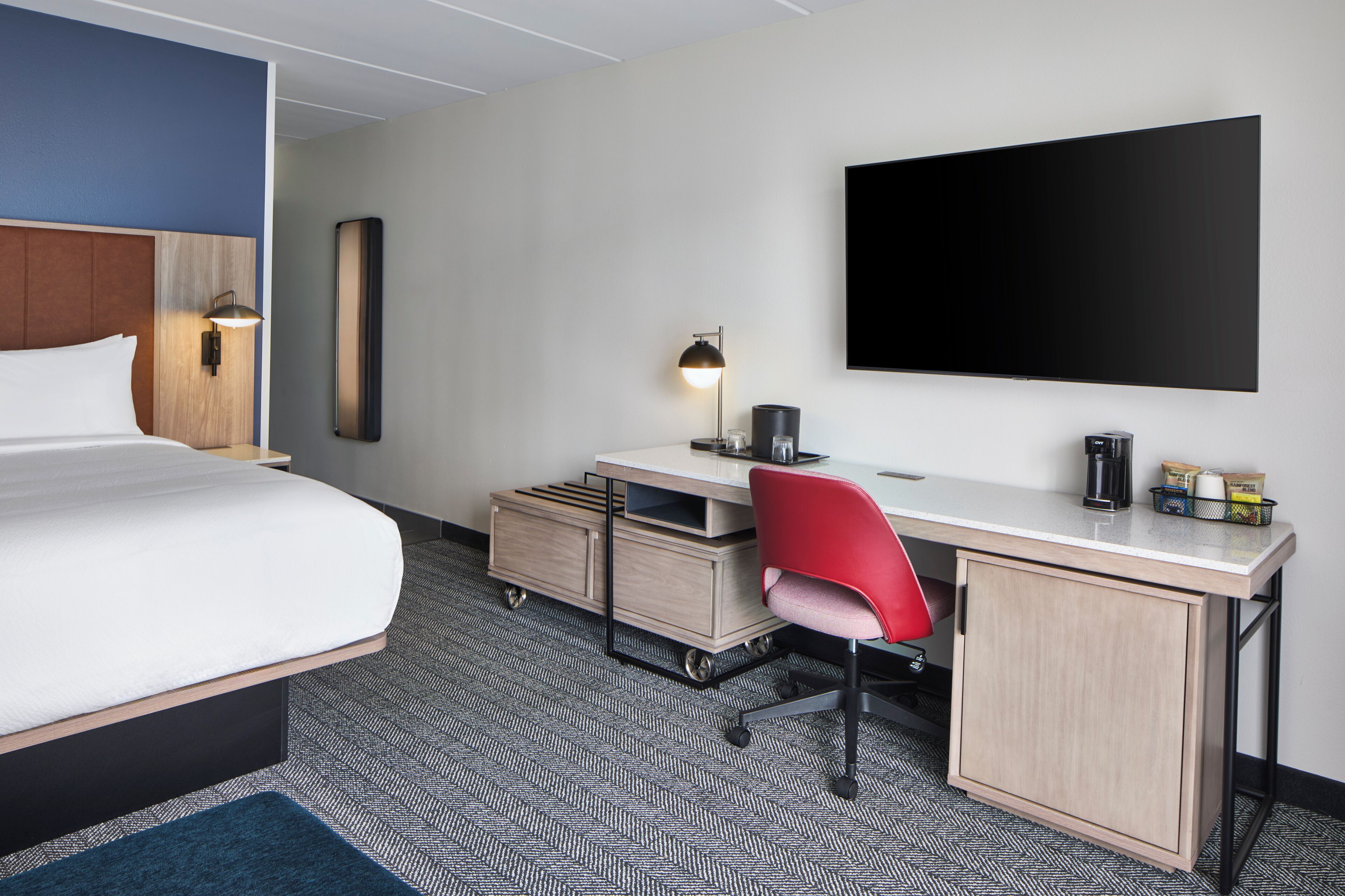 A hotel room with a bed, desk, chair, and a flat-screen TV.