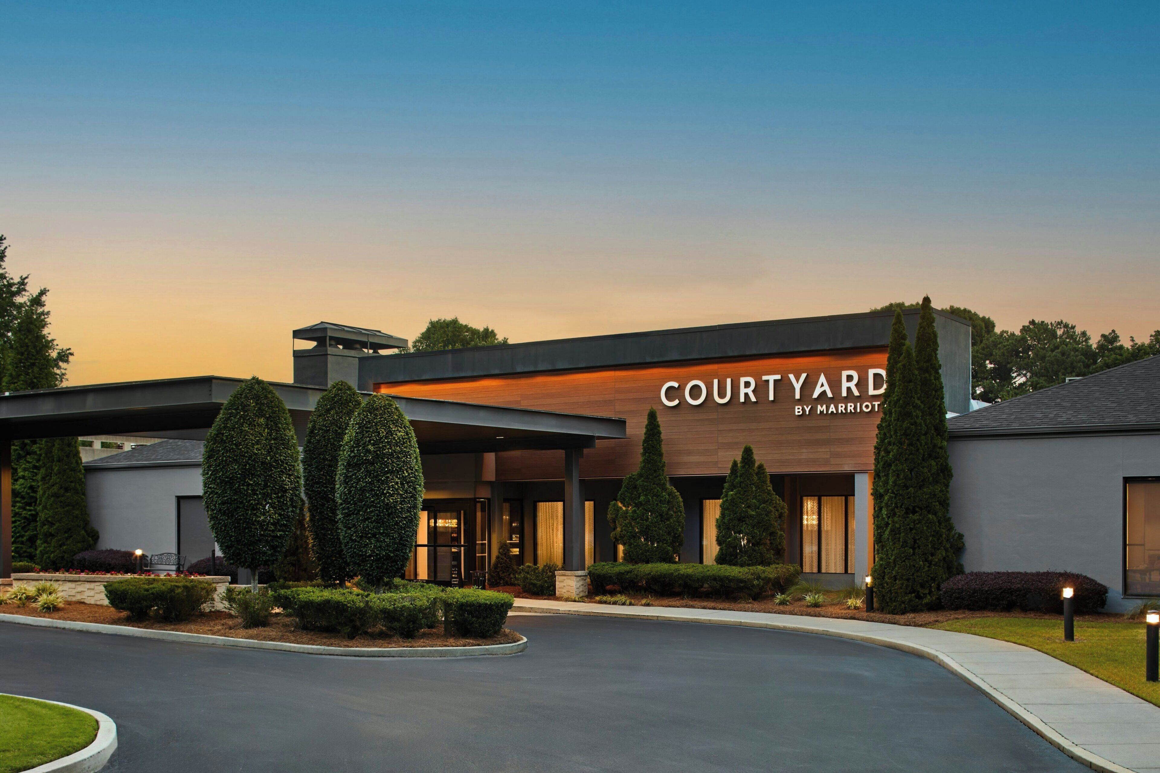 Un hotel Courtyard by Marriott con diseño moderno, que presenta una entrada cubierta y jardines bien cuidados.