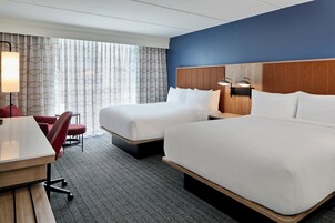Habitación de hotel con dos camas, un escritorio, una silla y una ventana con cortinas.