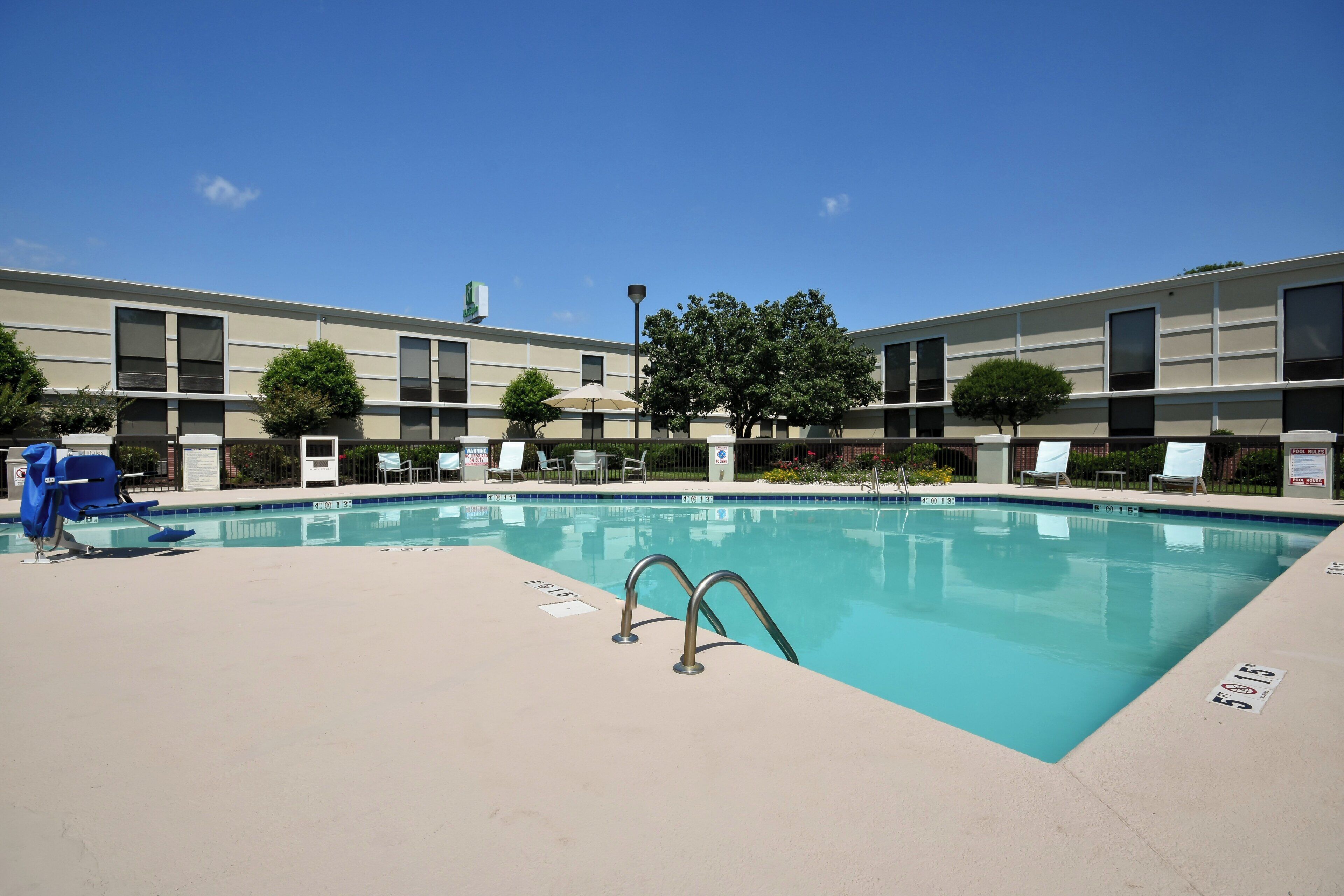 A swimming pool with a lifeguard stand, lounge chairs, and a building with a sign in the background.