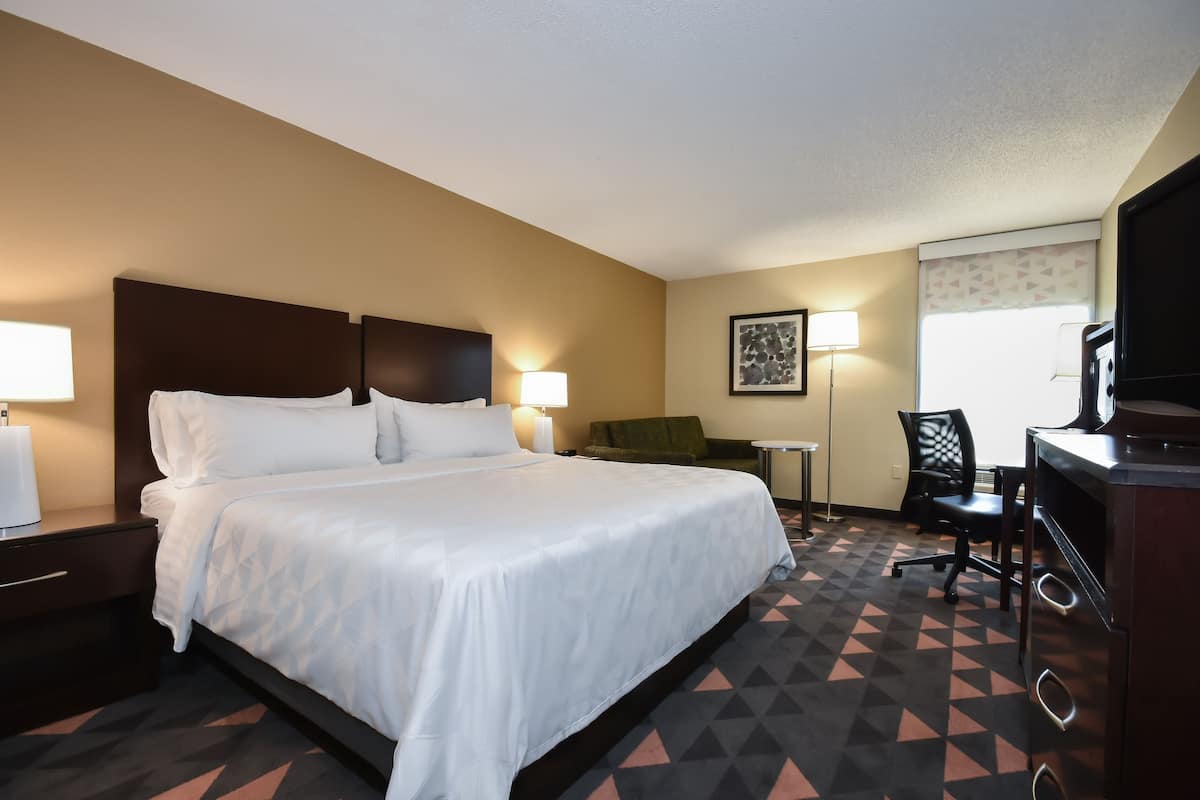 A hotel room with a large bed, bedside lamps, a desk with a chair, and a television.