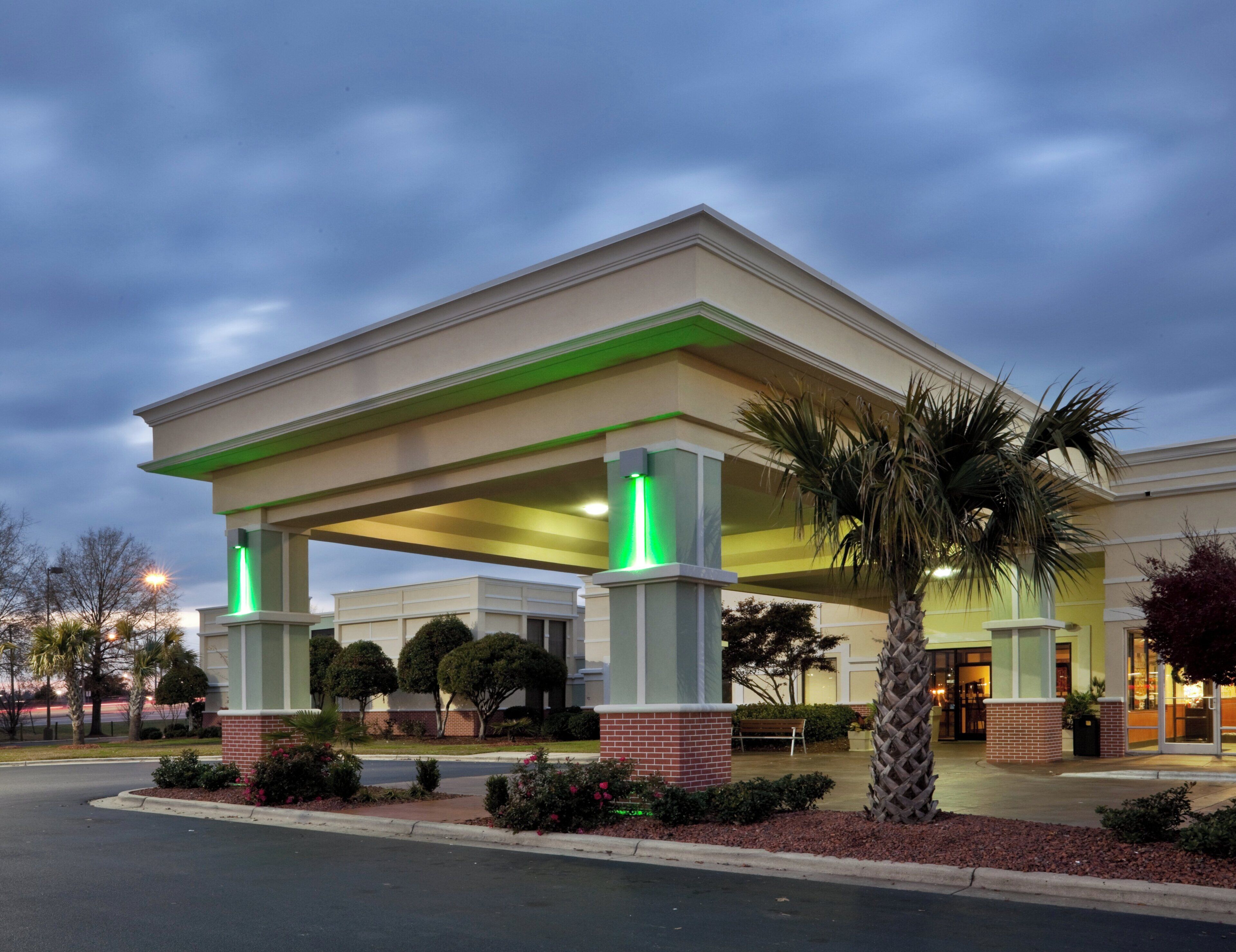 A hotel entrance with a covered patio, palm trees, and a brick facade.