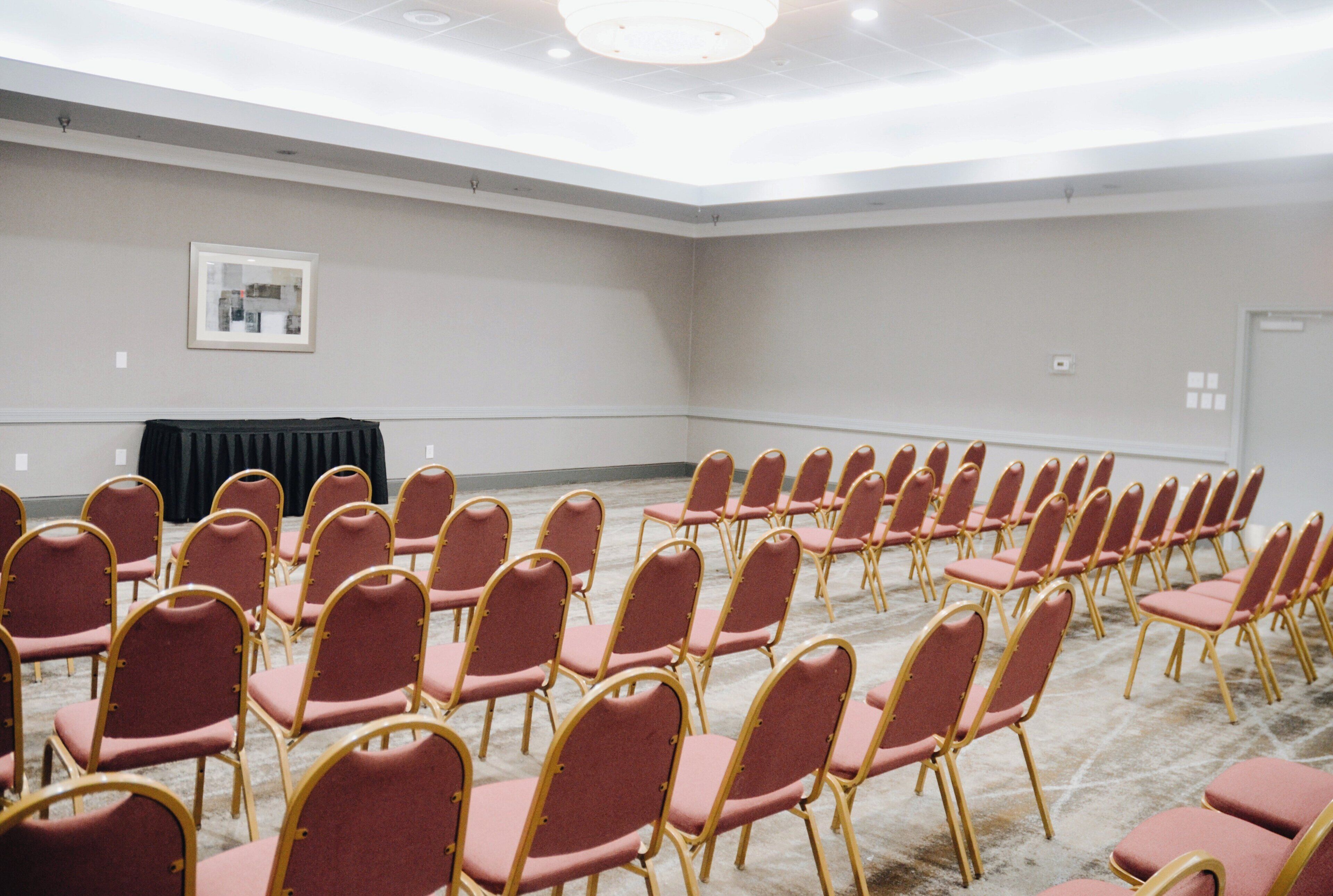 A conference room with rows of red chairs and a black table.