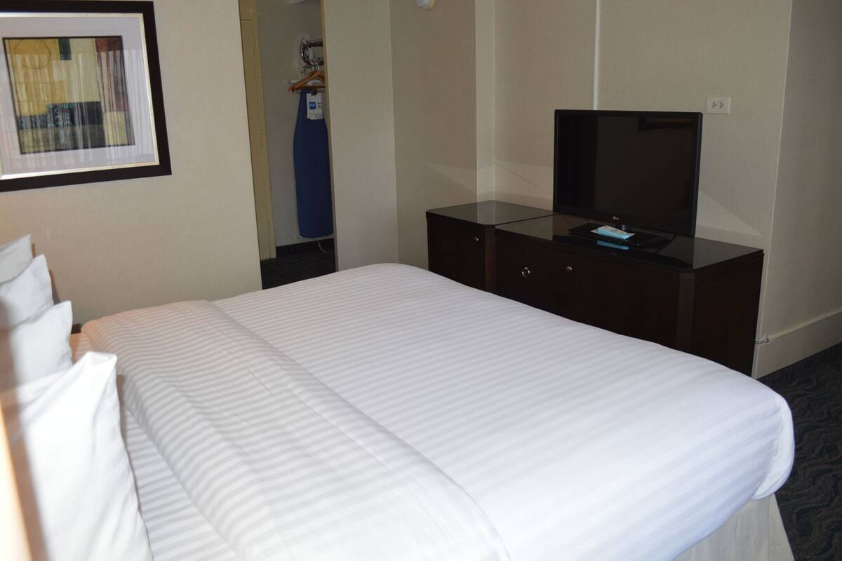 A hotel room with a bed, a TV on a dresser, and a framed picture on the wall.