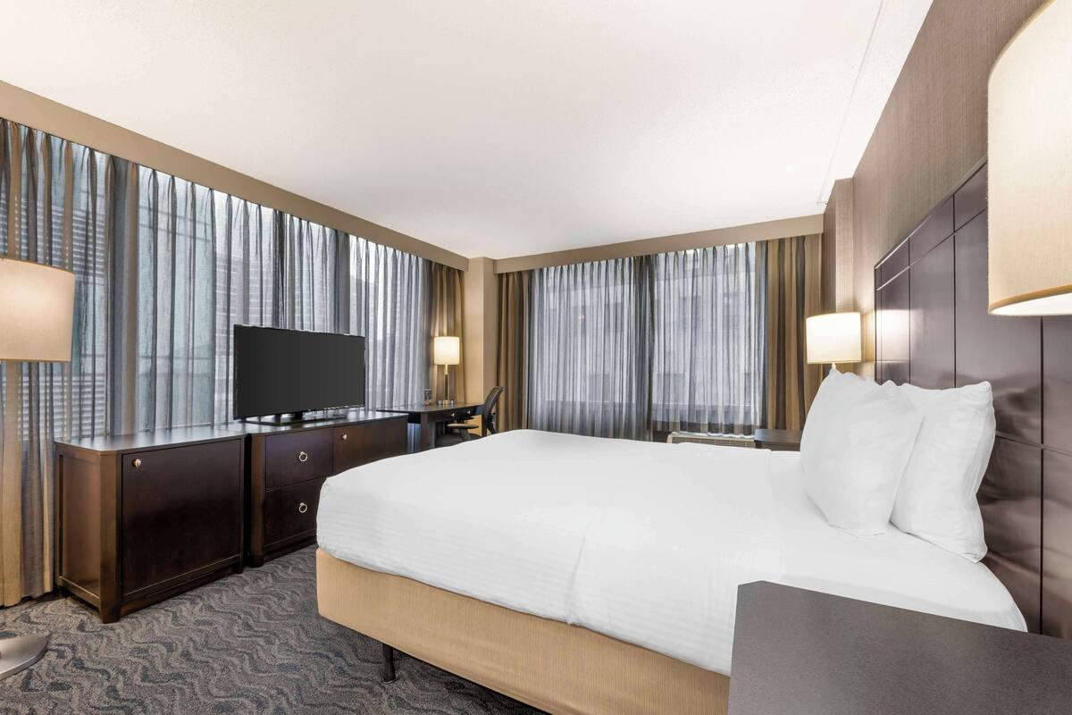 A hotel room with a large bed, a desk, a television, and curtains.