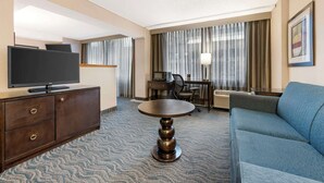 A hotel room with a flat-screen TV, a wooden cabinet, a round table, a blue sofa, a desk with a computer, and a large window with curtains. - Best Western Grant Park Hotel (Chicago)