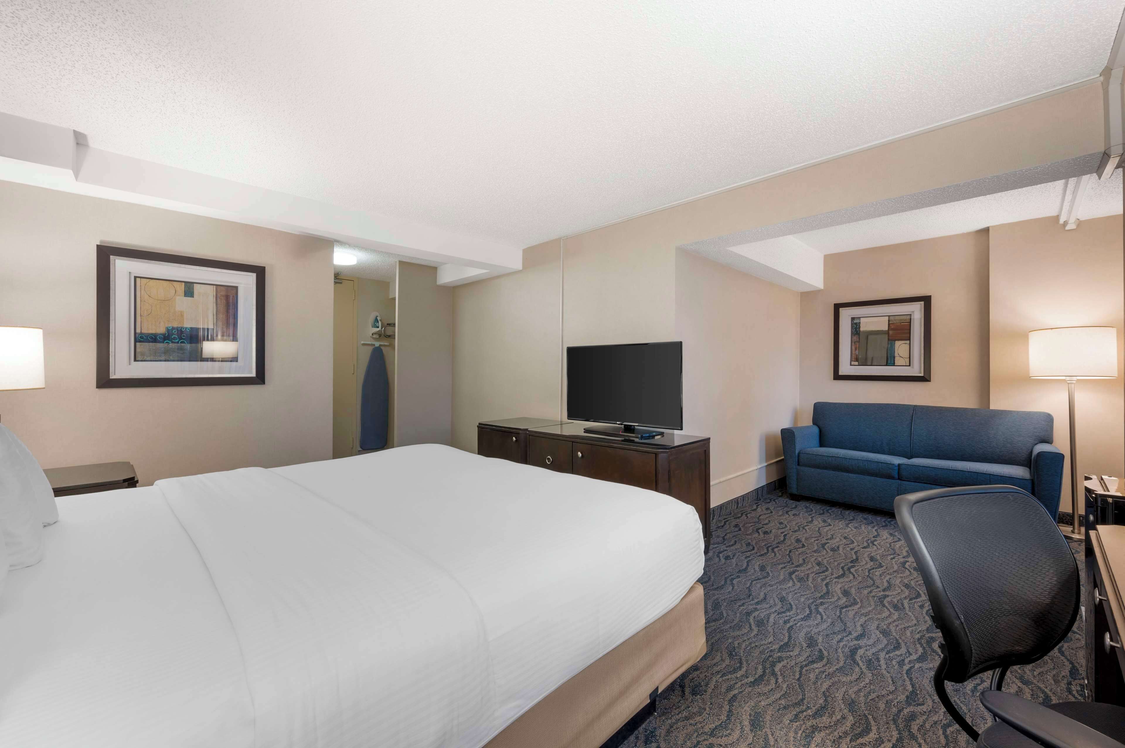 A hotel room with a large bed, a TV on a wooden dresser, a blue sofa, and a desk with a lamp.