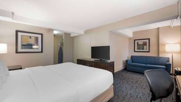 A hotel room with a large bed, a TV on a wooden dresser, a blue sofa, and a desk with a lamp.