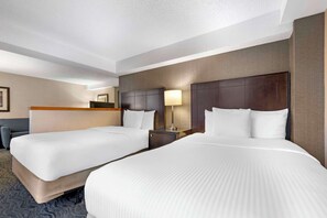 A hotel room with two beds, a desk, a chair, and a lamp.