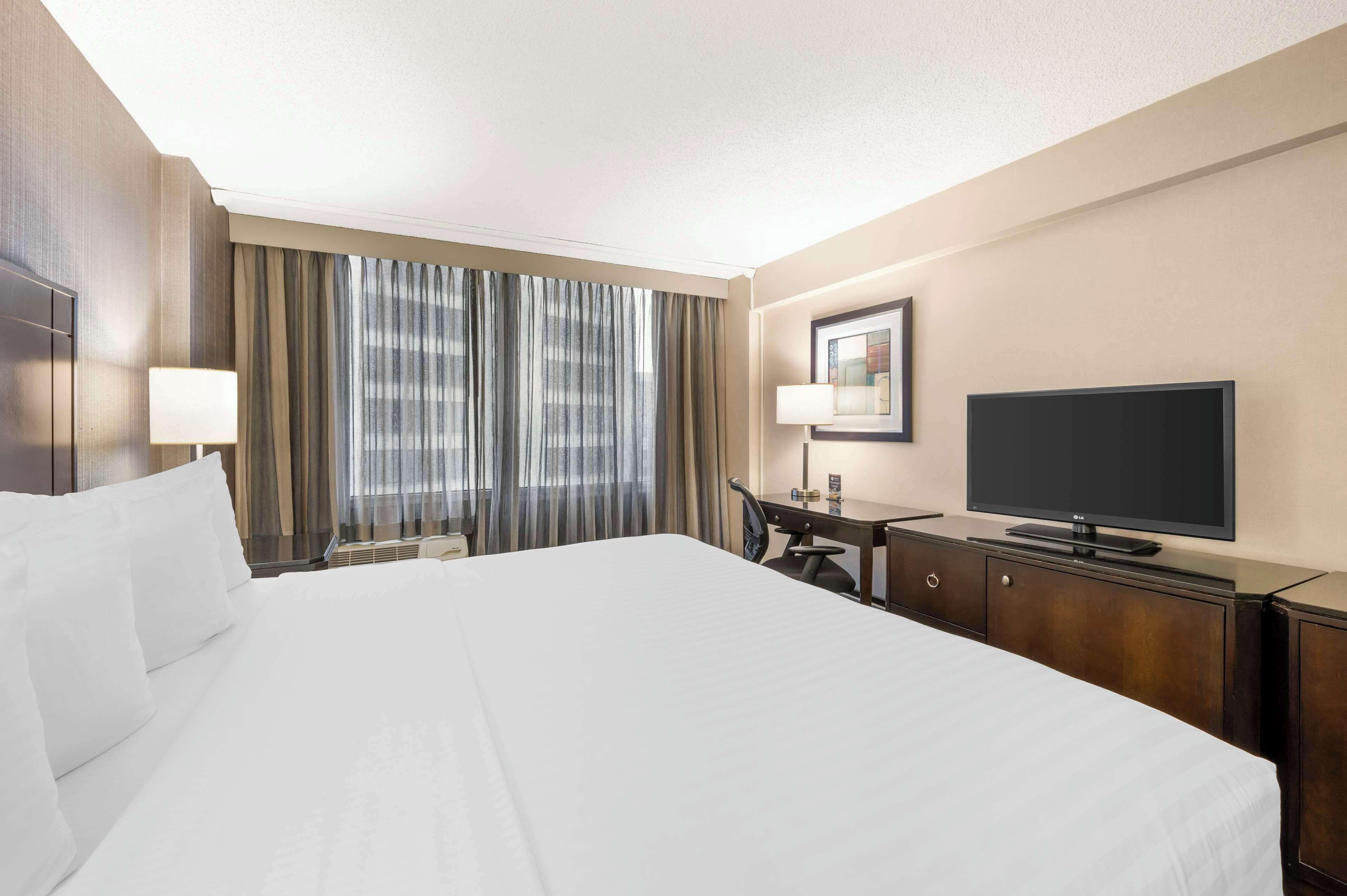 A hotel room with a large bed, a desk with a chair, a television, and a window with curtains.