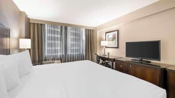 Een hotelkamer met een groot bed, een bureau met stoel, een televisie en een raam met gordijnen.