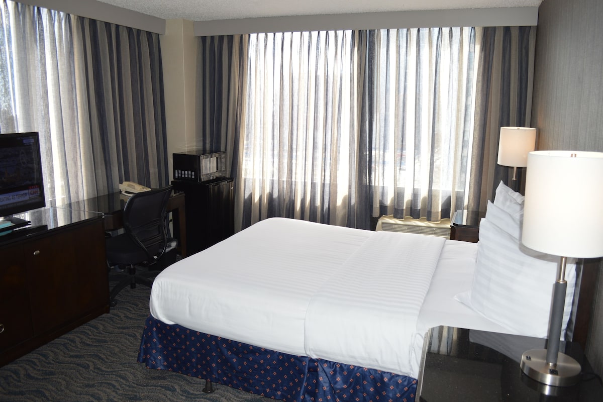 Een hotelkamer met een bed, een bureau met telefoon, een stoel, een televisie en gordijnen.