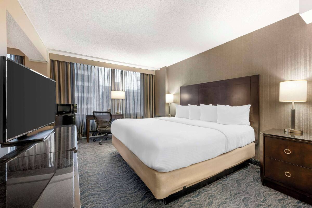 A hotel room with a large bed, a flat-screen TV, a desk with a lamp, and a chair.