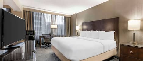 A hotel room with a large bed, a flat-screen TV, a desk with a lamp, and a chair.