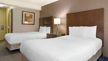 A hotel room with two beds, a nightstand with a lamp, and a framed picture on the wall.