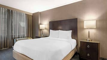 Une chambre d’hôtel avec un grand lit, deux tables de chevet avec des lampes, une grande fenêtre avec des rideaux et un sol recouvert de moquette.