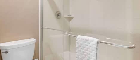Un baño con cabina de ducha de vidrio, un inodoro blanco y un toallero con una toalla blanca.