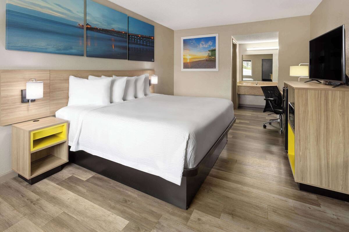 Habitación de hotel con una cama grande, un escritorio con televisión, una silla y obras de arte en las paredes.