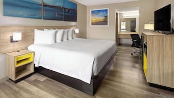 A hotel room with a large bed, a desk with a TV, a chair, and artwork on the walls.