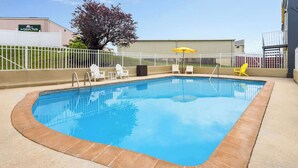 Una piscina rectangular amb un videtell daurat, envoltada per una tanca blanca i un parasol groc.