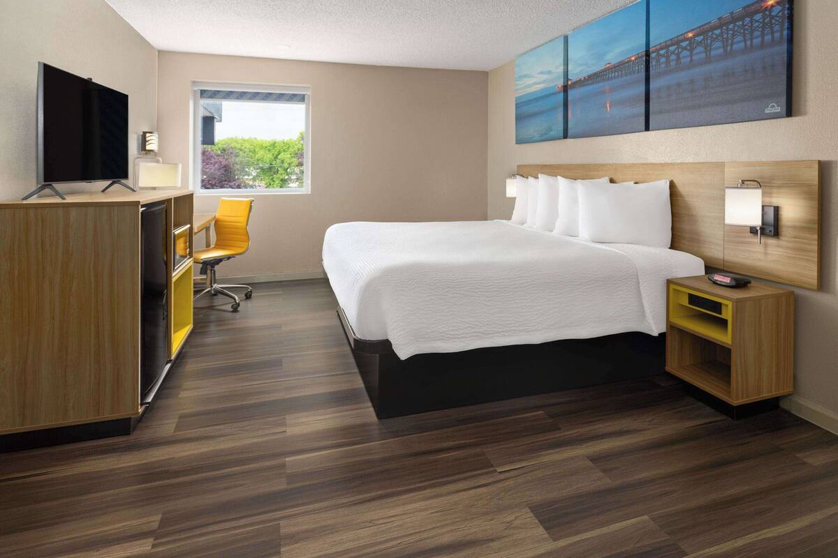Habitación de hotel moderna con una cama grande, un escritorio con computadora, una silla y una ventana con vista a la vegetación.