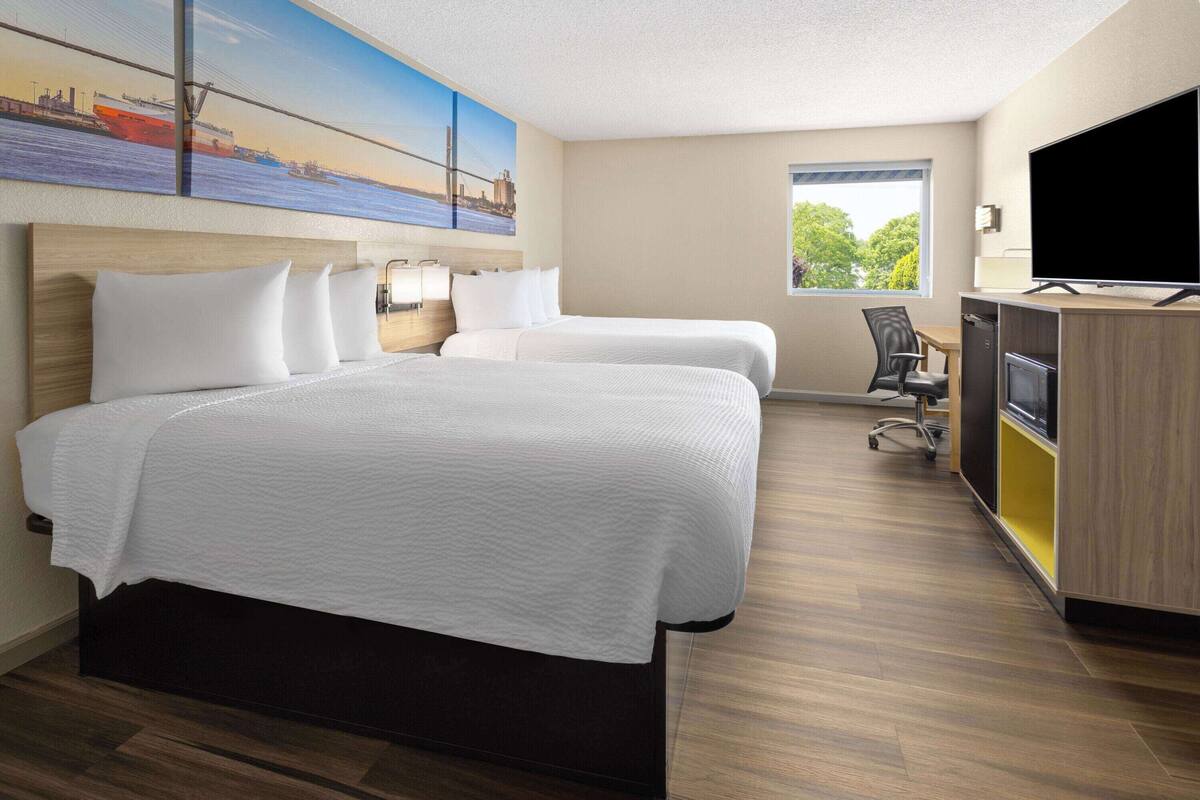 Habitación de hotel con dos camas, un escritorio, un televisor de pantalla plana, una silla y una ventana con vista a árboles.