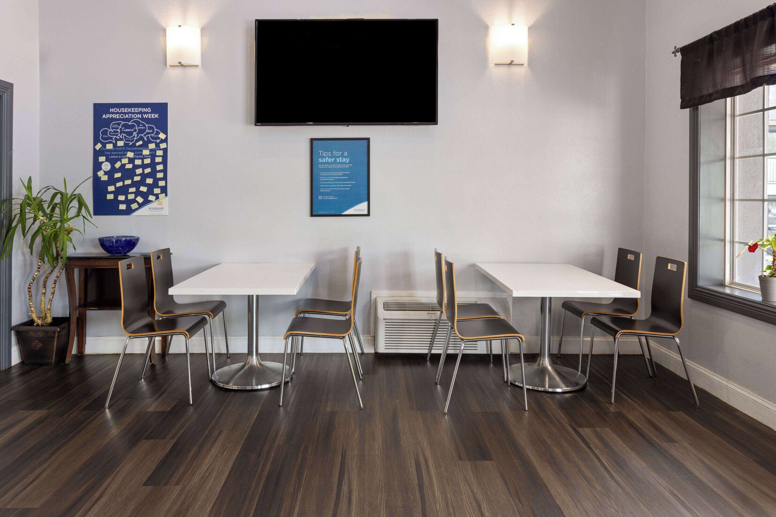 A conference room with a white table, four chairs, a flat-screen TV, and two posters on the wall.