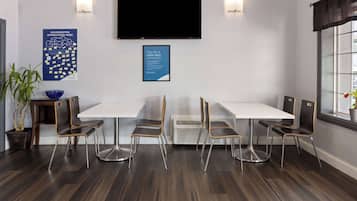 A conference room with a white table, four chairs, a flat-screen TV, and two posters on the wall.