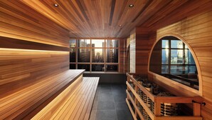 A sauna with wooden walls and benches, a large arched window, and a view of buildings. - The Westin Calgary (Calgary)