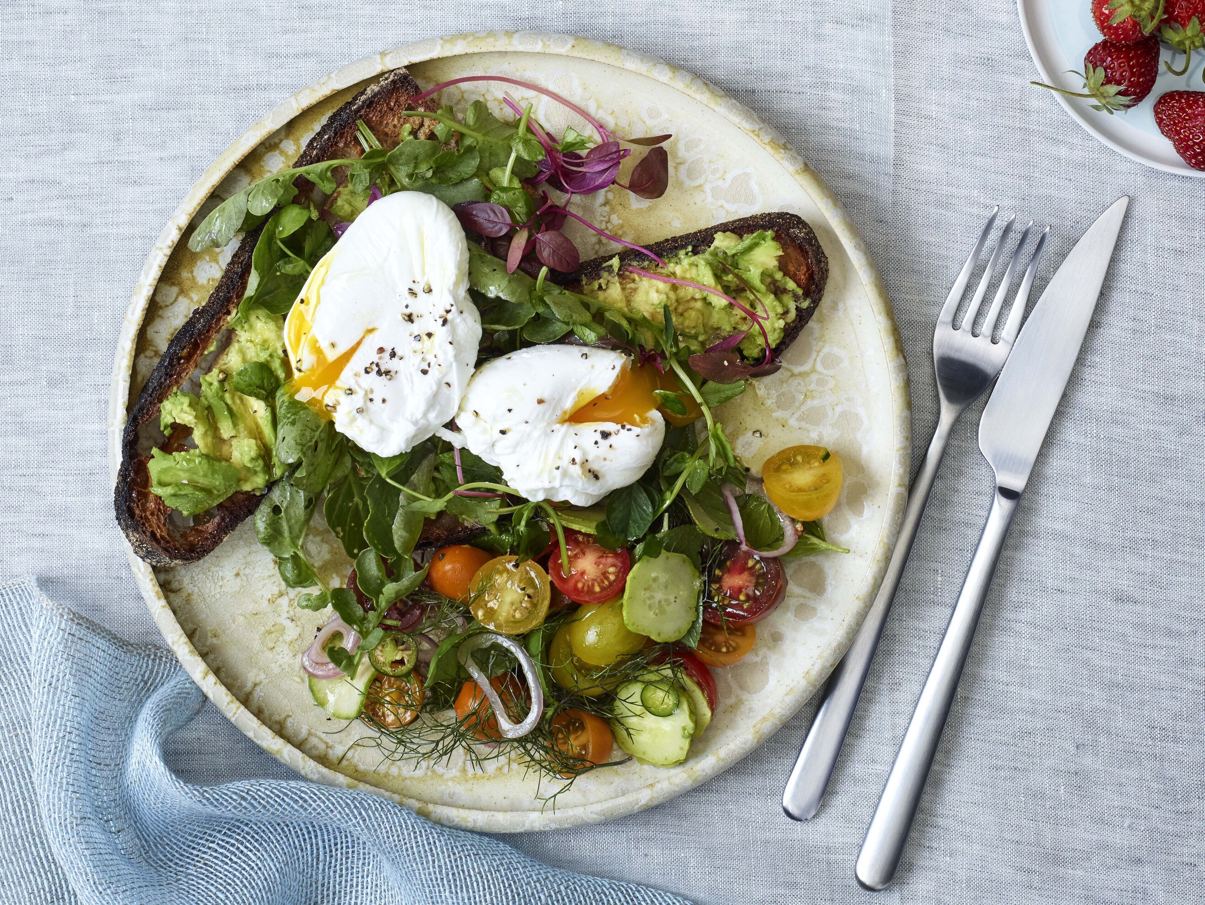 A plate of food with a salad, poached eggs, and avocado on toast.