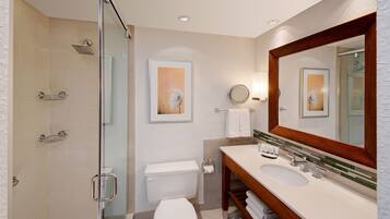 A modern bathroom with a glass-enclosed shower, a white toilet, a sink with a wooden vanity, and a large mirror.