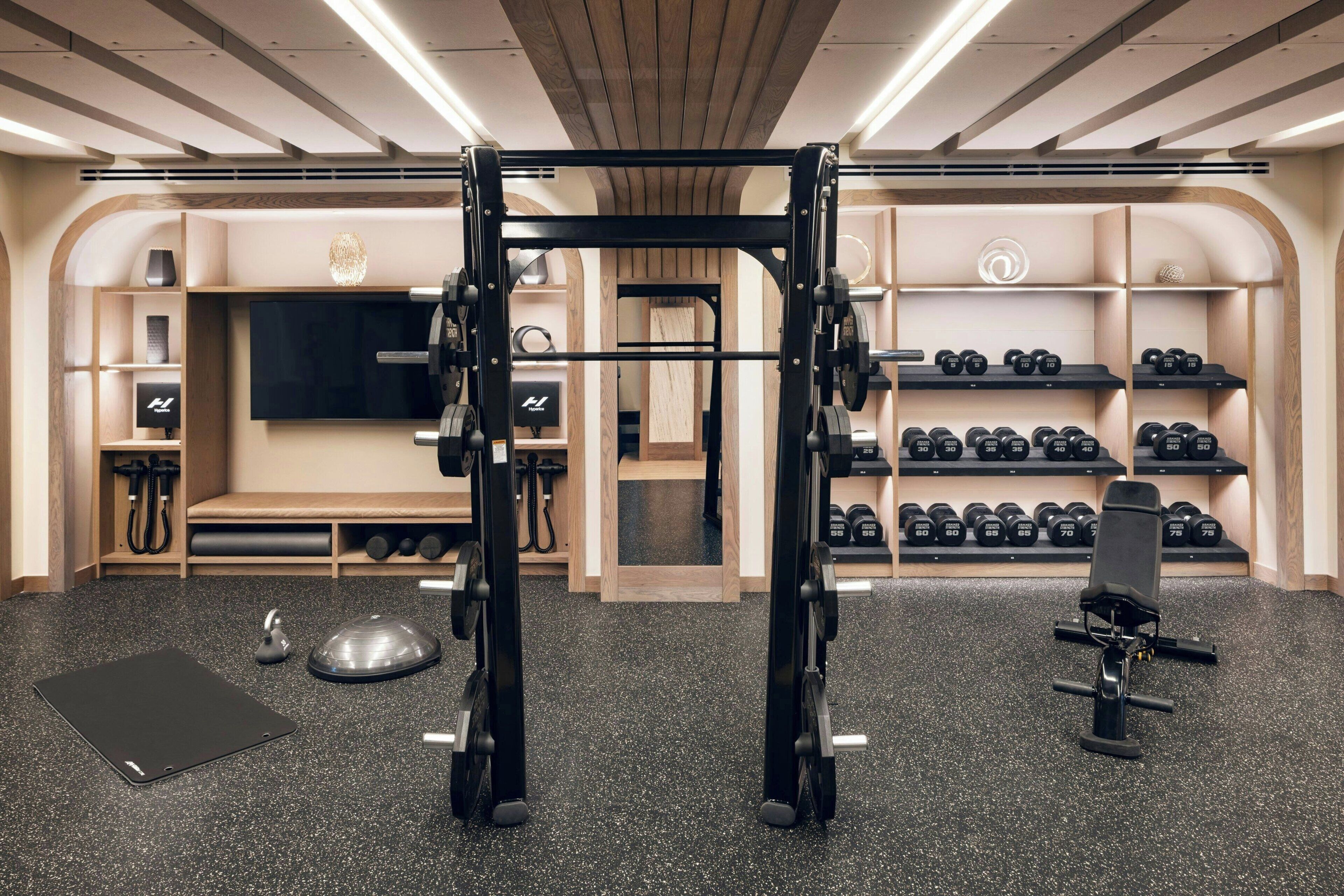 Ein Fitnessraum mit einer Klimmzugstange, Hanteln, einer Bank und einem Fernseher.