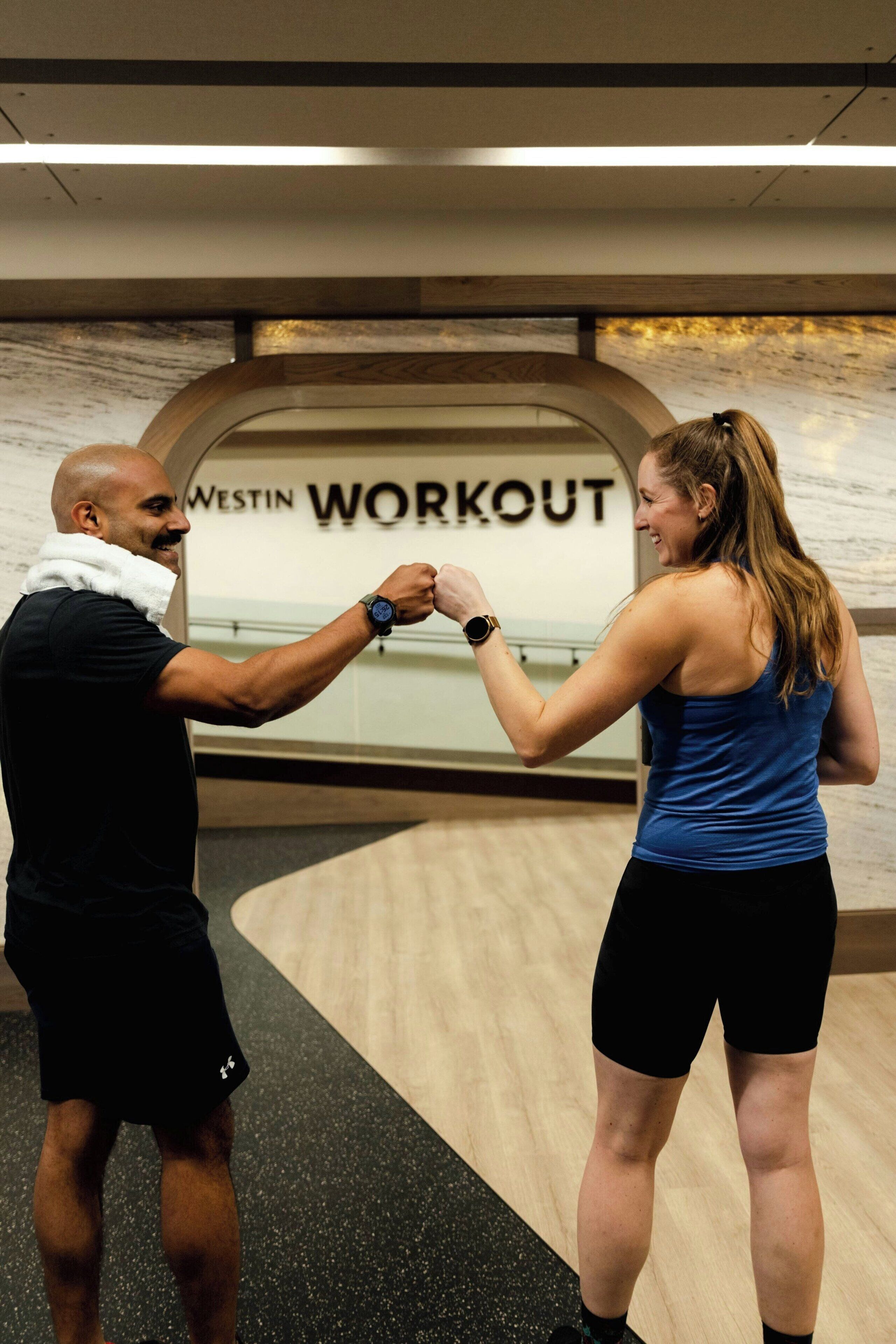 Dos personas en un gimnasio, con un letrero que dice 'Westin Workout'.