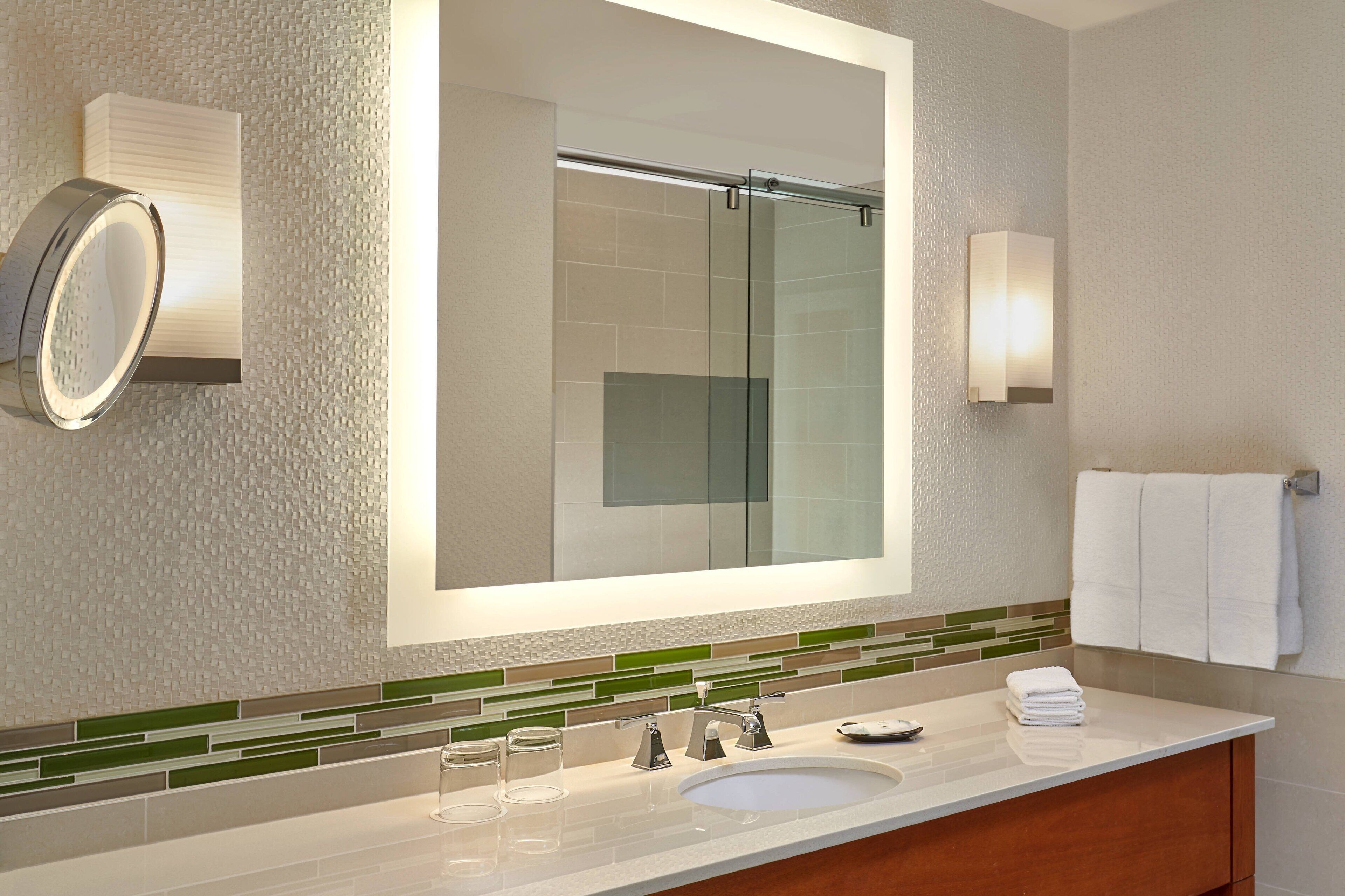 A modern bathroom with a large mirror, a sink, and a glass shower enclosure.