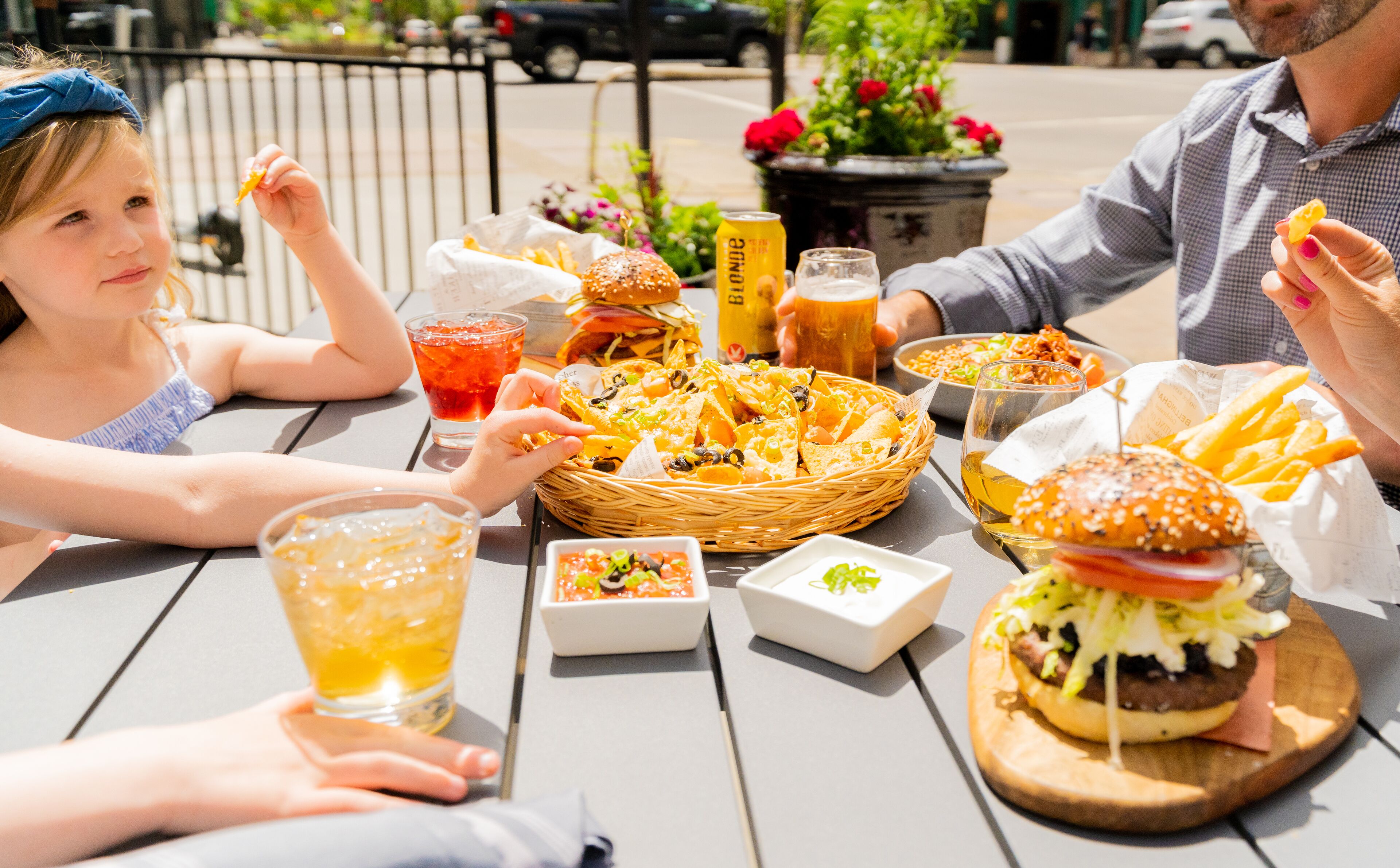 Una mesa de comedor con comida y bebidas, incluyendo hamburguesas, papas fritas y una bebida en un vaso.