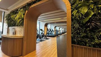 Ein Fitnessraum mit Holzboden, Trainingsgeräten und einer Wand mit Grünpflanzen.