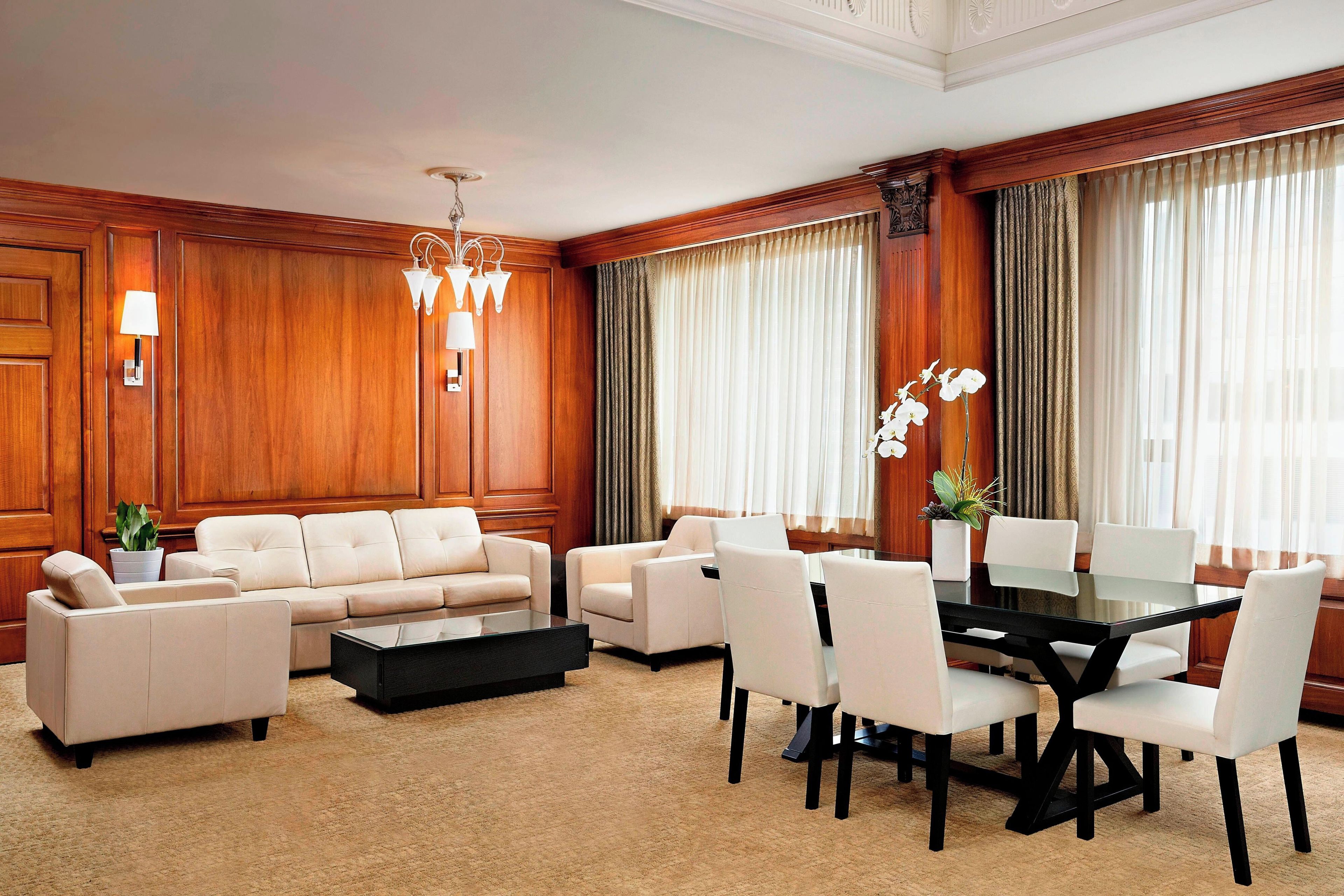 A hotel room with a sofa set, a dining table with chairs, a coffee table, and a potted plant.