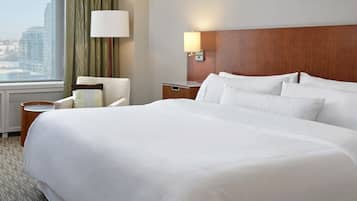 Habitación de hotel con una cama grande, una mesita de noche, una lámpara, una silla y vistas a la ciudad.