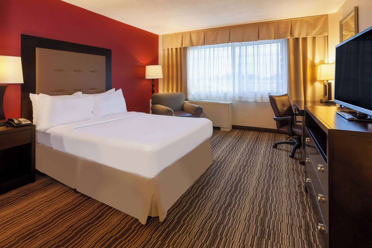 A hotel room with a large bed, a desk with a television, a chair, and a desk lamp.