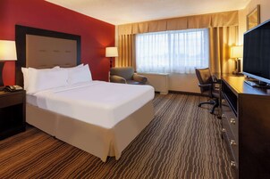 Habitación de hotel con una cama grande, un escritorio con televisor, una silla y una lámpara de escritorio.