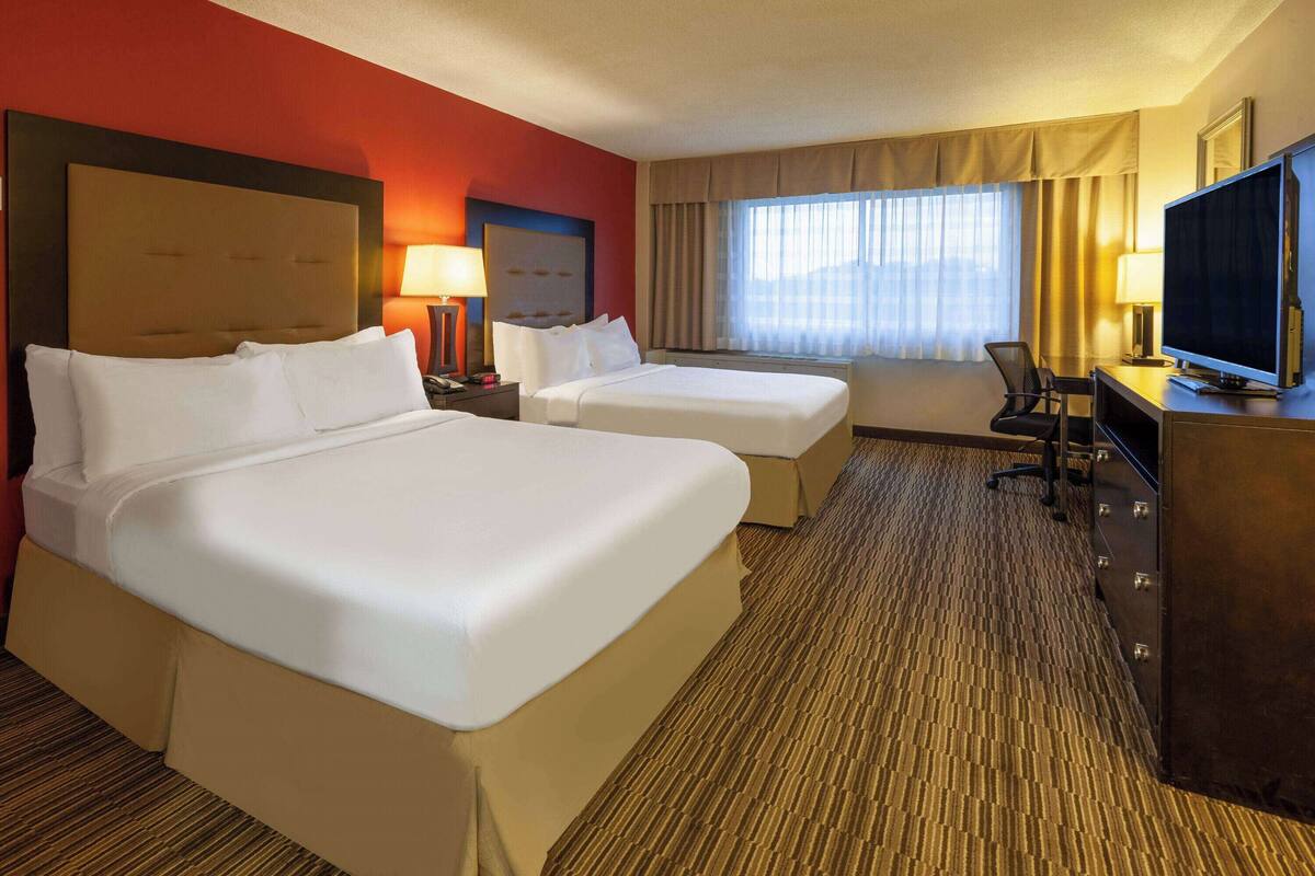 A hotel room with two beds, a desk with a television, and a window with curtains.