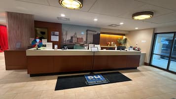 A hotel reception desk with a cityscape mural, a digital screen, and a black mat with "RH" on it.