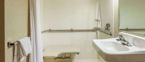 Un baño con lavamanos blanco, ducha con cabezal de ducha de mano, toallero y espejo.
