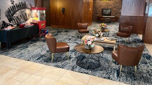 Un hall d’hôtel avec un tapis à motifs noir et blanc, des fauteuils en cuir marron, un appareil à pop-corn et un mur en pierre sur lequel est accrochée une télévision.