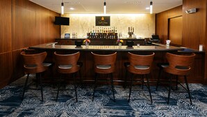 Un espace bar doté d’un comptoir en marbre, de plusieurs tabourets de bar, d’un téléviseur fixé au mur et d’un assortiment de bouteilles et de verres.