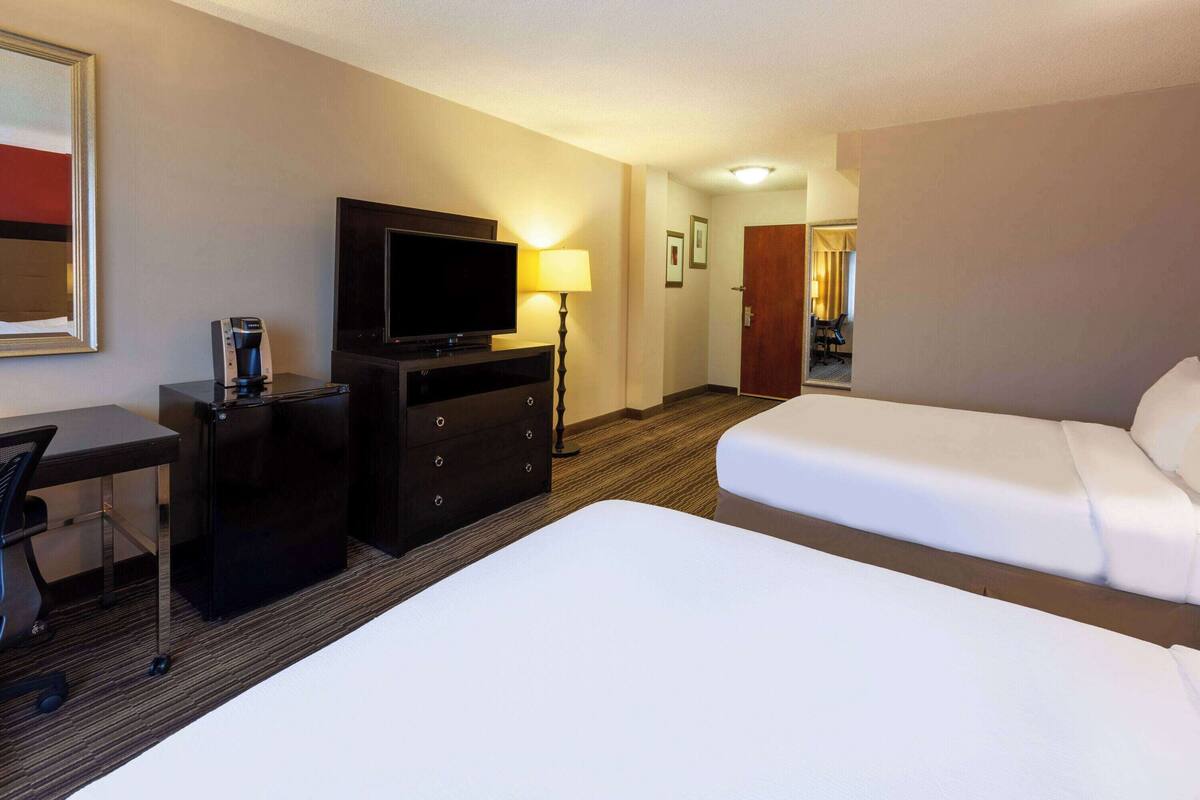 A hotel room with two beds, a desk with a chair, a television, and a coffee maker.