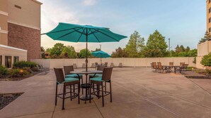 Un espace extérieur aménagé en terrasse, avec des tables et des chaises, de grands parasols, et un bâtiment en briques en arrière-plan.
