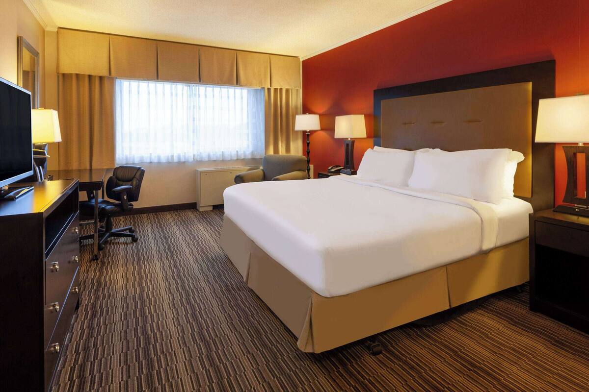 A hotel room with a large bed, a desk with a TV, two chairs, and a window with curtains.