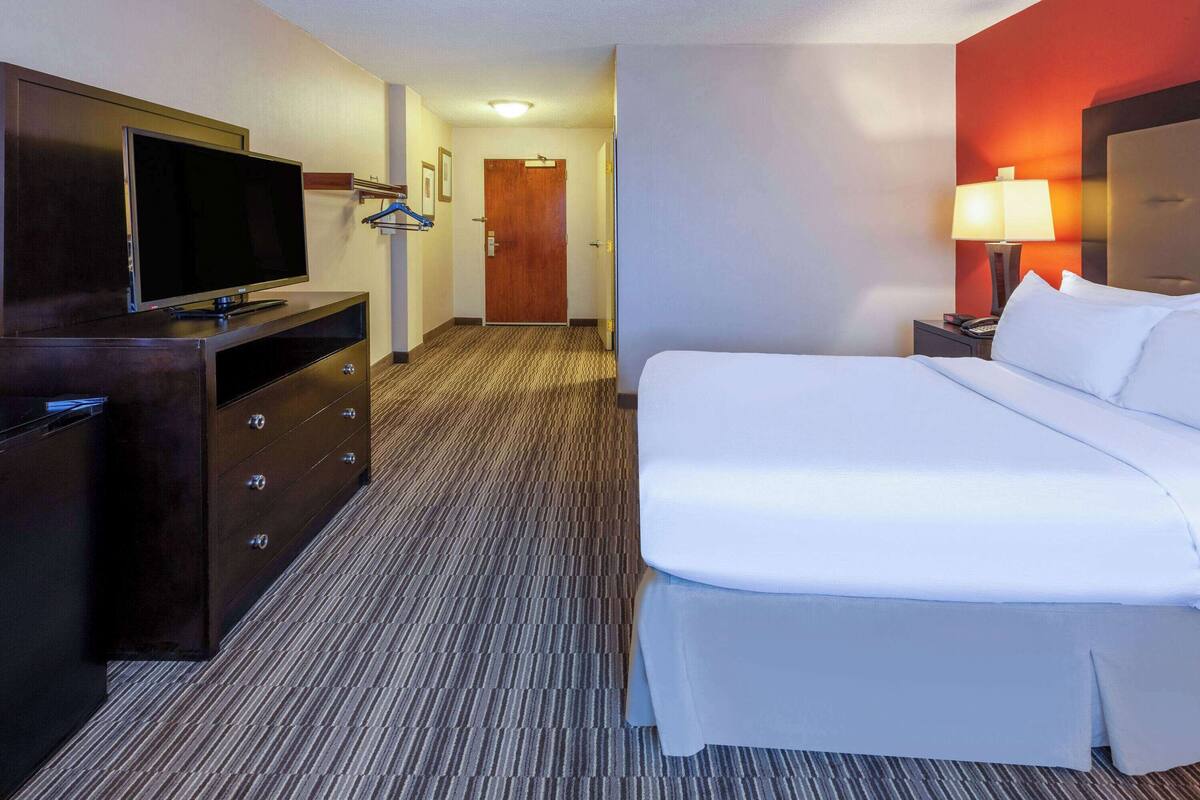 A hotel room with a bed, a TV on a dresser, a lamp, and a door.