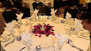 A round dining table set for a formal meal with white tablecloths, silverware, and glassware.